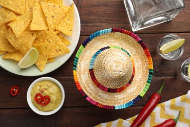 Mexican sombrero hat, tequila with lime, chili peppers, nachos chips and dip sauce on wooden table, flat lay