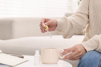 Woman dripping food supplement into cup on white table indoors, closeup