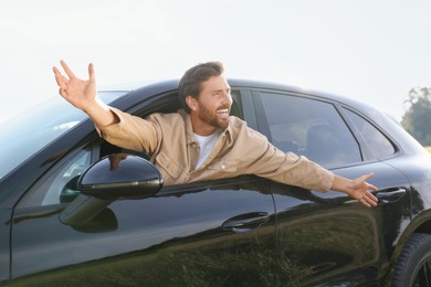 Photo of Enjoying trip. Happy man leaning out of car window outdoors