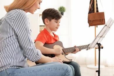 Photo of Little boy playing guitar with his teacher at music lesson. Learning notes