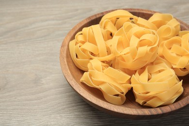 Raw tagliatelle pasta in bowl on light grey wooden table, closeup. Space for text