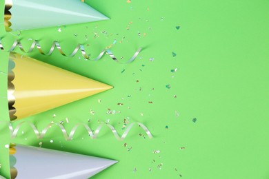 Bright party hats, serpentine streamers and confetti on green background, flat lay