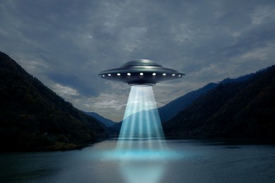 Image of Alien spaceship emitting light beam in air over lake. UFO