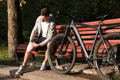 Photo of Man with injured knee on bench near bicycle outdoors