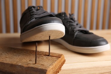 Photo of Nails in wooden plank and shoes on table, closeup