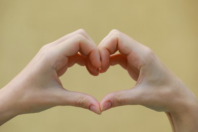 Photo of Woman making heart with hands on beige background, closeup