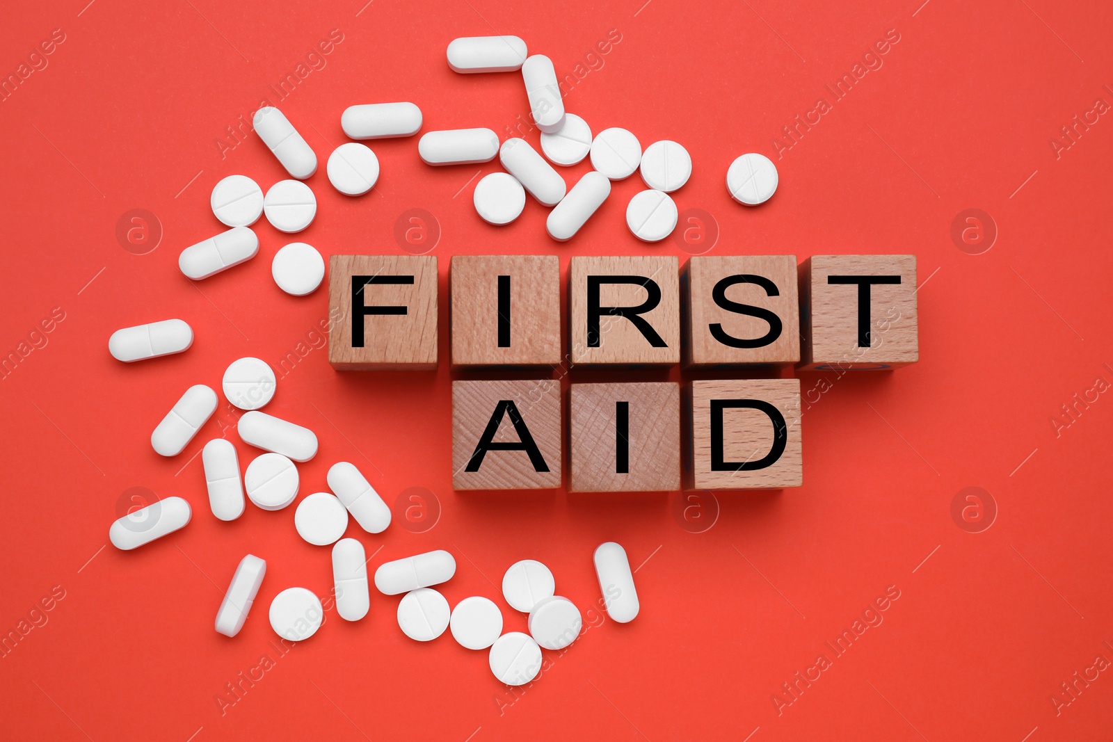 Photo of Words First Aid made of wooden cubes and pills on coral background, flat lay