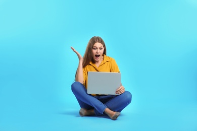 Photo of Emotional young woman with laptop celebrating victory on color background