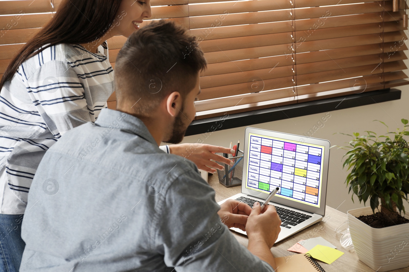 Photo of Colleagues working with calendar app on laptop in office