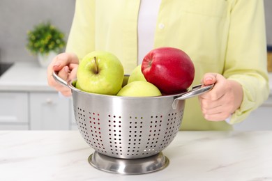 Photo of Woman holding colander with fresh apples at white marble table in kitchen, closeup