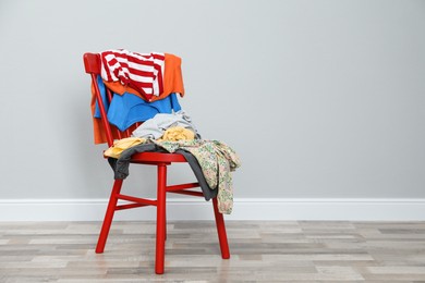 Different clothes on red chair near grey wall, space for text