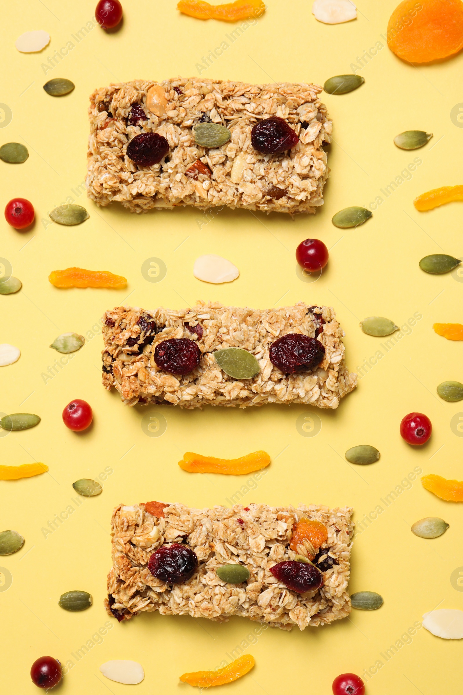 Photo of Tasty granola bars and ingredients on yellow background, flat lay