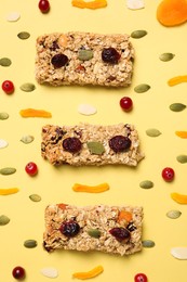 Tasty granola bars and ingredients on yellow background, flat lay