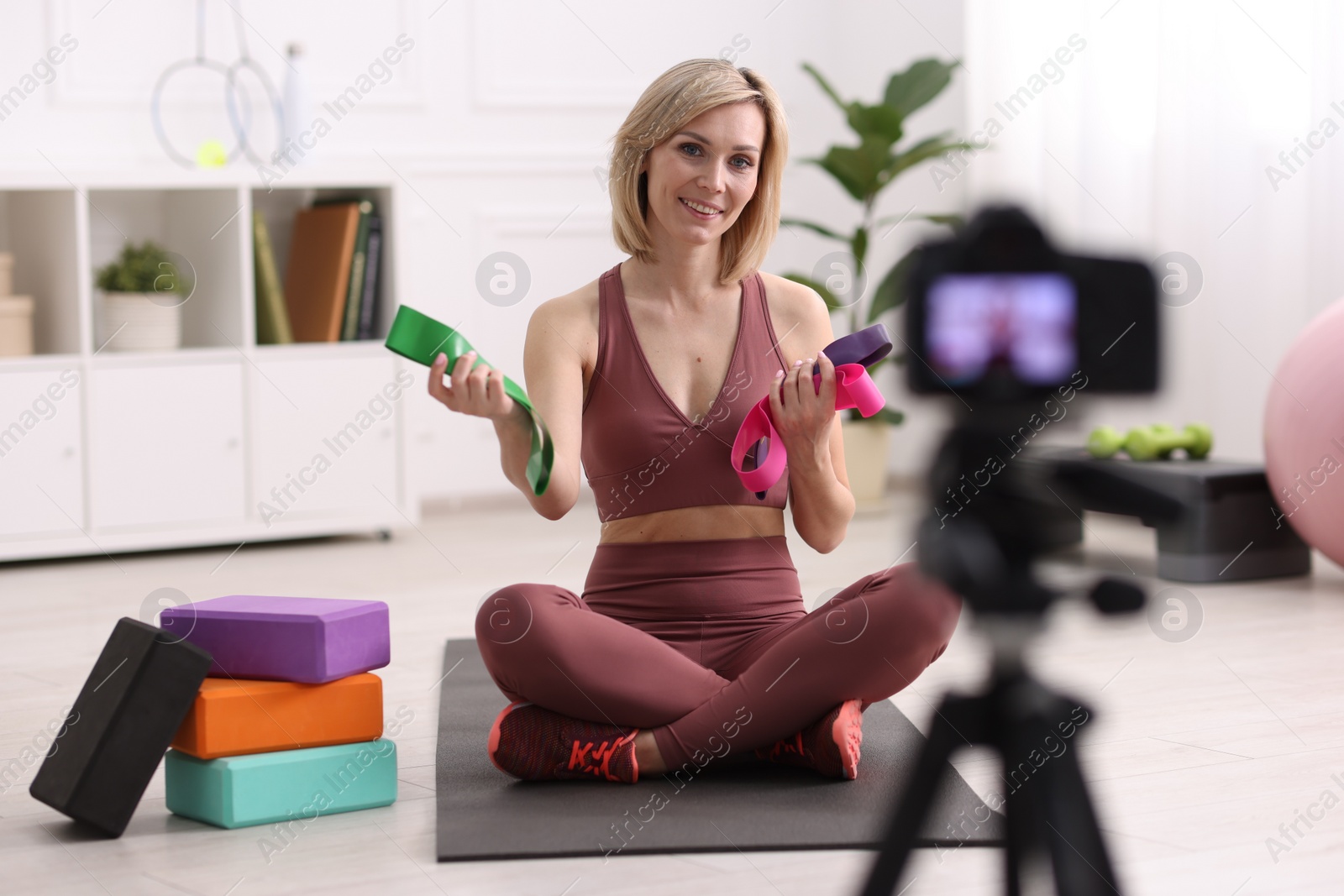 Photo of Smiling sports blogger with with resistance bands recording fitness lesson with camera at home