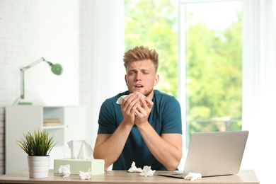 Photo of Young man suffering from allergy at home office