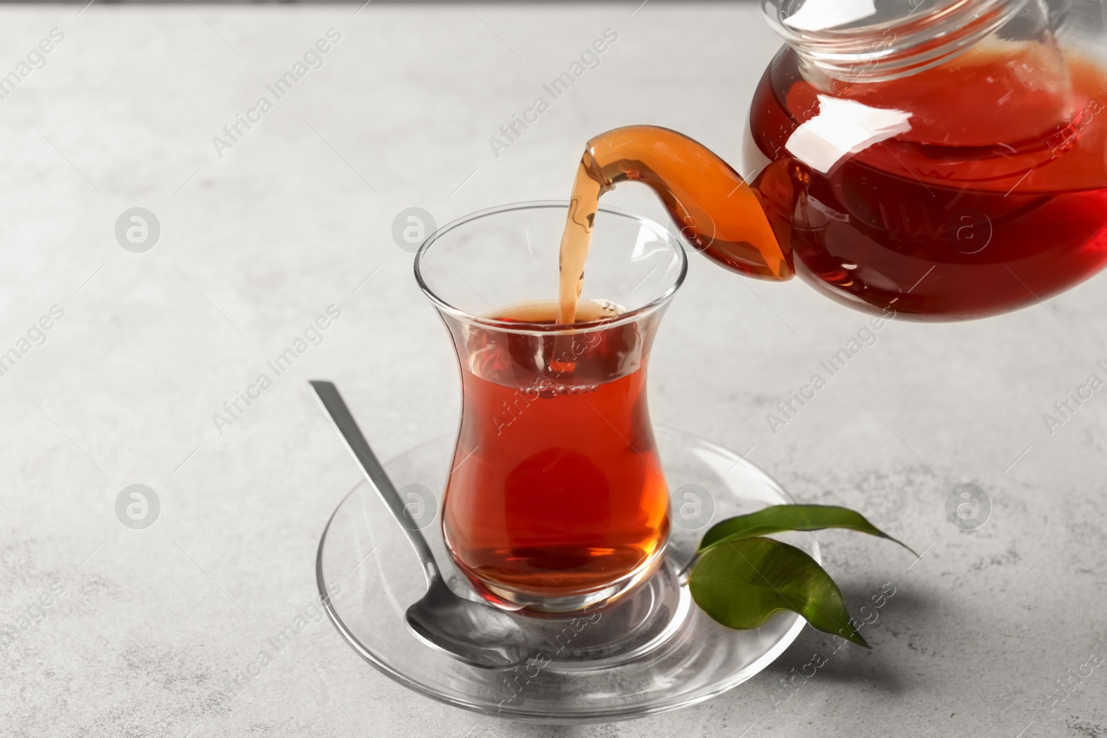 Photo of Pouring traditional Turkish tea from pot into glass on light grey table