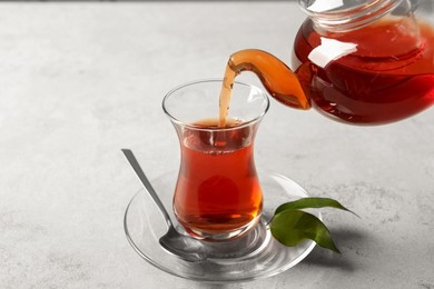 Pouring traditional Turkish tea from pot into glass on light grey table