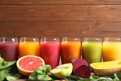 Photo of Glasses with different juices and fresh ingredients on wooden background