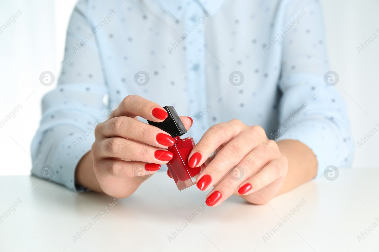 Photo of Woman with bottle of bright nail polish at white table, closeup