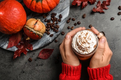 Woman holding mason jar of tasty pumpkin spice latte at grey table, top view