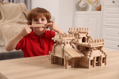 Photo of Cute little boy playing with wooden castle at table in room. Child's toy