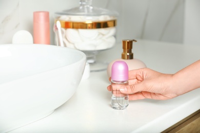 Photo of Woman holding roll-on deodorant in bathroom, closeup view