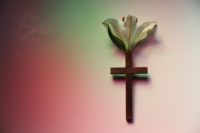 Wooden cross and lily flower on textured table in color lights, top view with space for text. Religion of Christianity