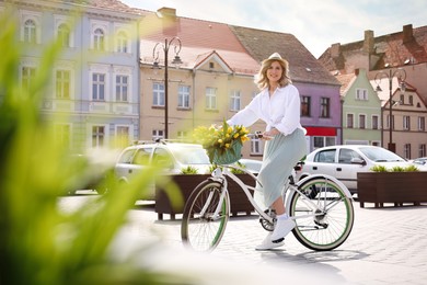 Beautiful woman with bicycle and bouquet of yellow tulips on city street