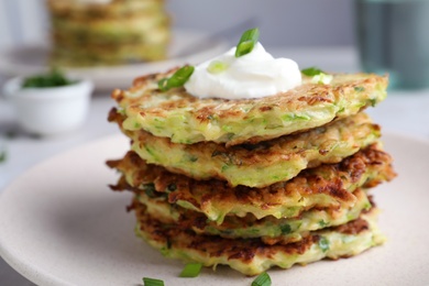 Photo of Delicious zucchini fritters with sour cream in plate, closeup view