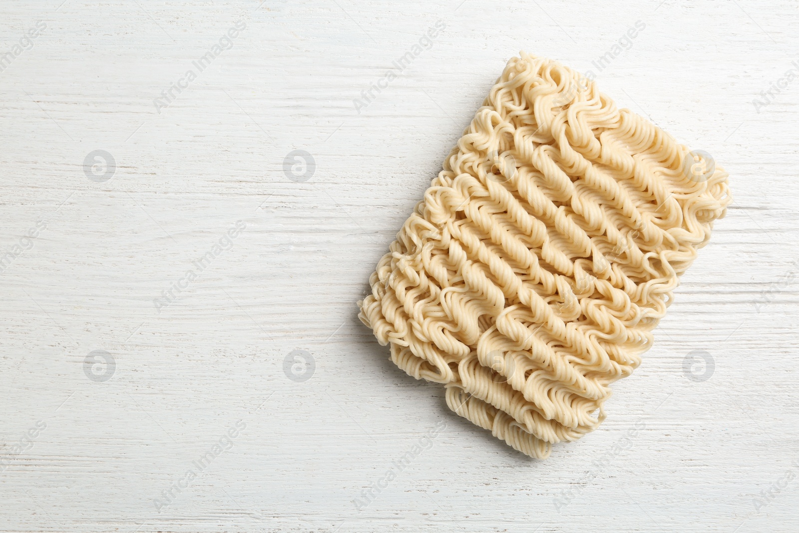 Photo of Block of quick cooking noodles on wooden background, top view. Space for text