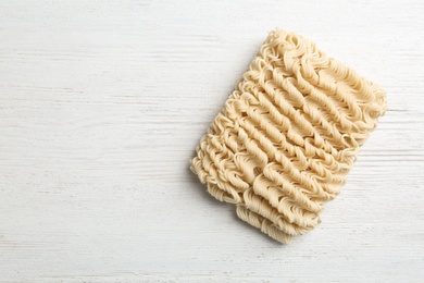 Photo of Block of quick cooking noodles on wooden background, top view. Space for text