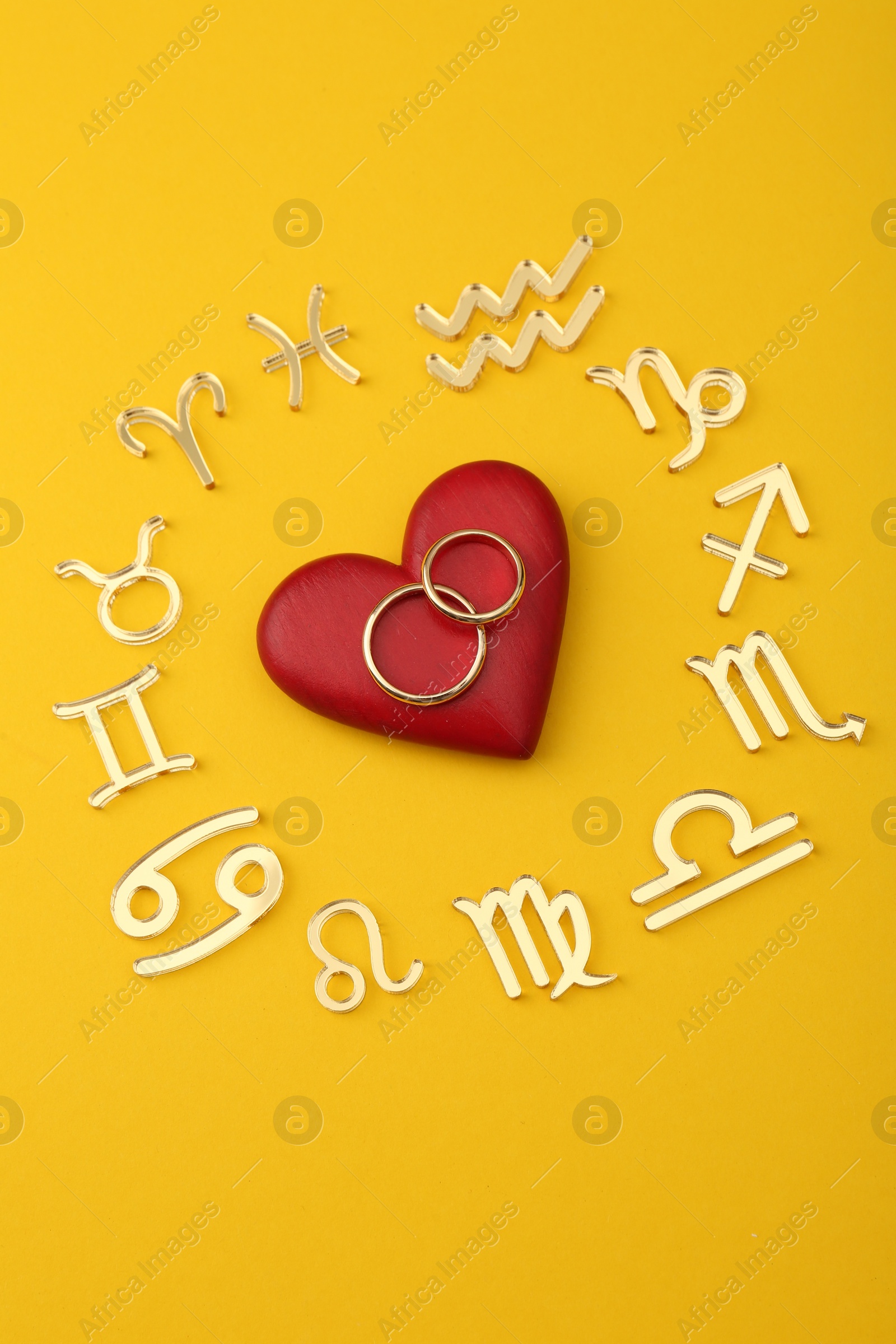 Photo of Zodiac signs, red heart and wedding rings on yellow background, flat lay