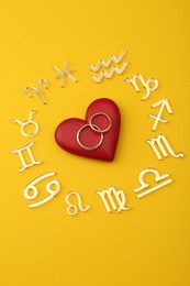 Photo of Zodiac signs, red heart and wedding rings on yellow background, flat lay