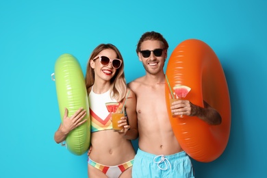 Photo of Happy young couple in beachwear with inflatable rings and cocktails on color background