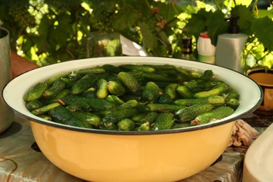 Photo of Fresh ripe cucumbers with water in metal bowl on table outdoors
