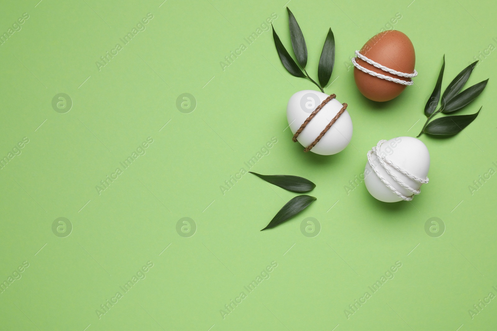 Photo of Beautifully decorated Easter eggs and leaves on light green background, flat lay. Space for text