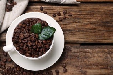 Photo of Cup with roasted coffee beans and leaves on wooden table, flat lay. Space for text