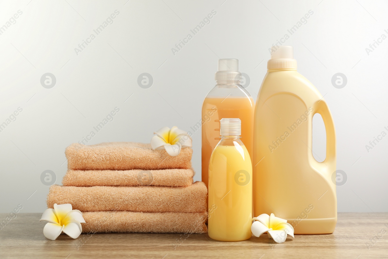 Photo of Bottles of laundry detergents, flowers and stacked fresh towels on table against white background