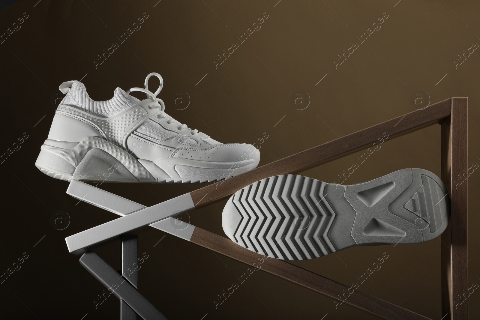 Photo of Pair of stylish white sneakers on brown background