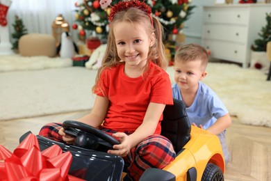 Photo of Cute little boy pushing toy car with his sister in room decorated for Christmas
