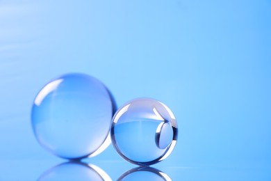 Photo of Transparent glass balls on mirror surface against blue background. Space for text