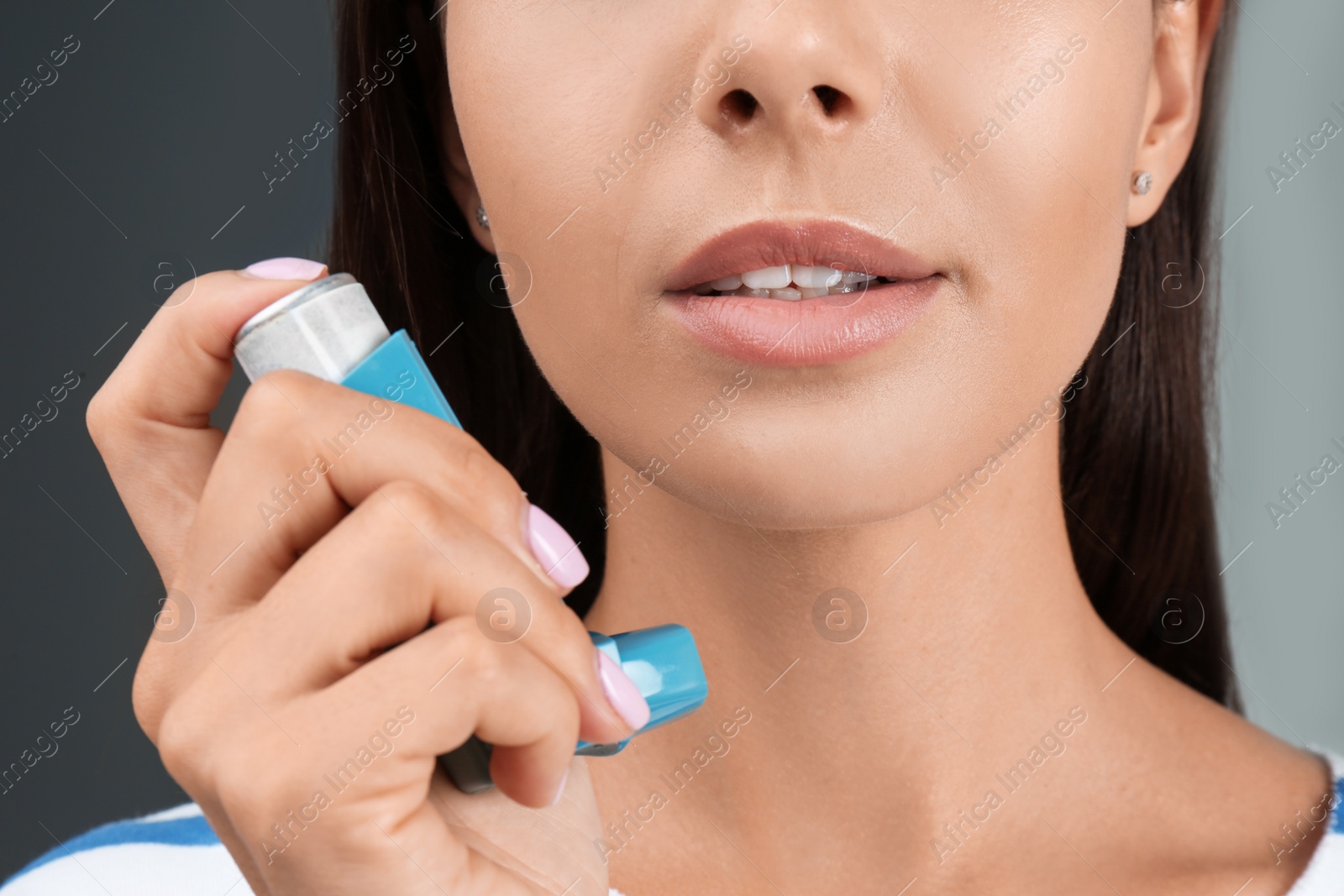 Photo of Young woman using asthma inhaler on color background, closeup