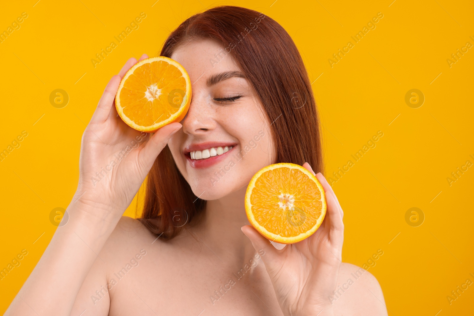 Photo of Smiling woman with freckles covering eye with half of orange on yellow background