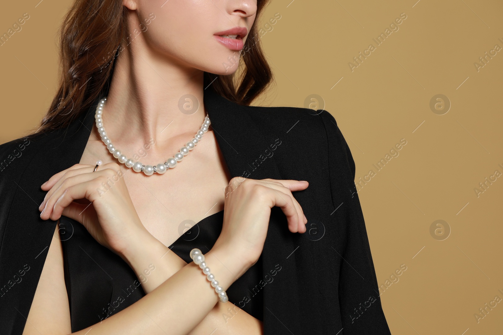 Photo of Young woman wearing elegant pearl jewelry on brown background, closeup