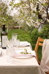 Stylish table setting with beautiful spring flowers, wine, plates and glasses in garden