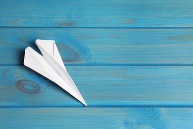 Handmade paper plane on light blue wooden table, top view. Space for text