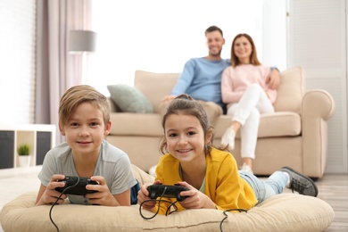 Cute children playing video games while parents resting on sofa at home