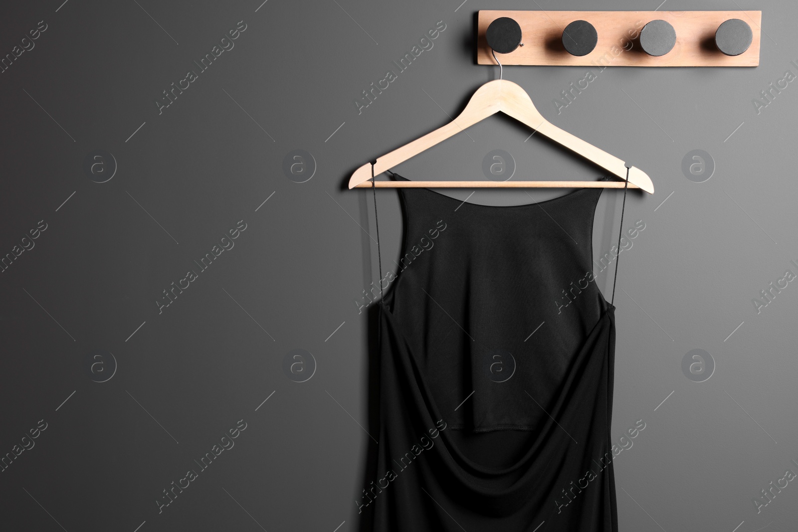 Photo of Beautiful black women's party dress on hanger near grey wall, space for text. Stylish trendy clothes for high school prom