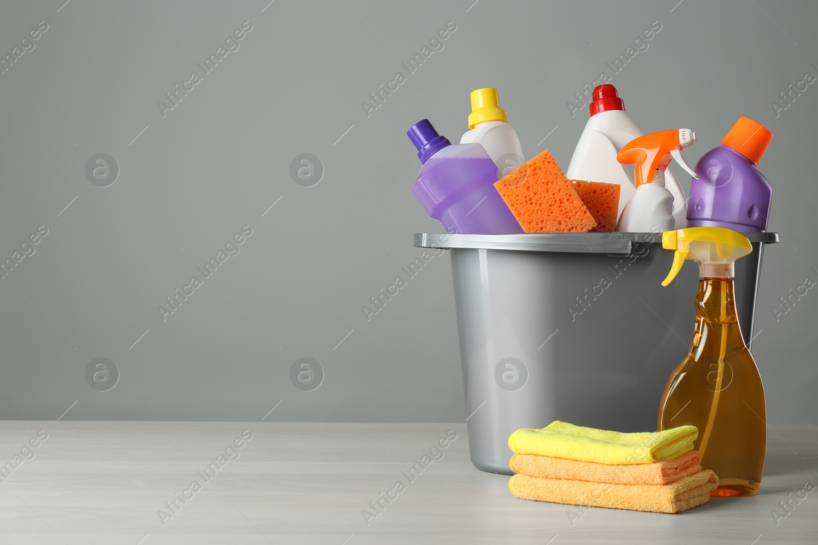 Photo of Bucket with cleaning products and tools on grey table. Space for text