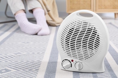 Photo of Electric fan heater and woman sitting on chair at home, closeup. Space for text